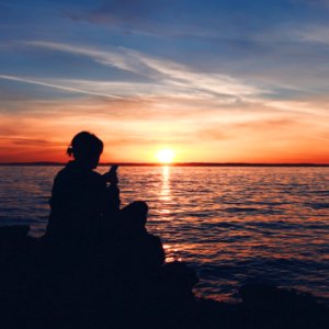 silhouette photo of person sitting on boulder near body of water photo