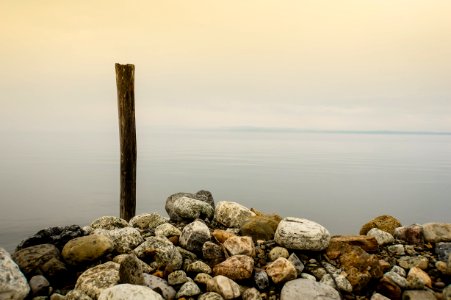 stones and brown wooden stick near body of water under cloudy sky photo