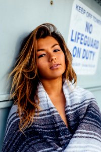 woman with black, white, and grey blanket leaning on wall with no lifeguard on duty signage photo