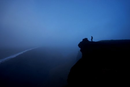 person standing rock cliff covered with fog