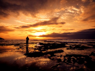 silhouette photo of man standing on beach during golden hour photo