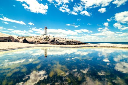 lighthouse tower near calm water under white clouds and blue sky photo