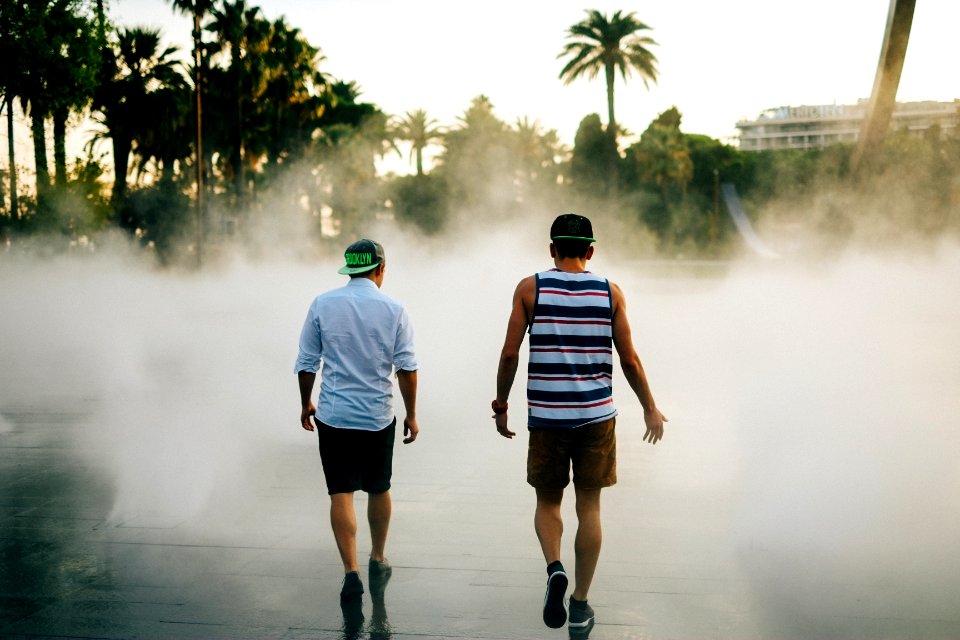 street photography of two men walking in front of water fountain