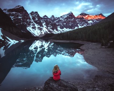 woman sitting on rock in front calm body of water and mountains view photo