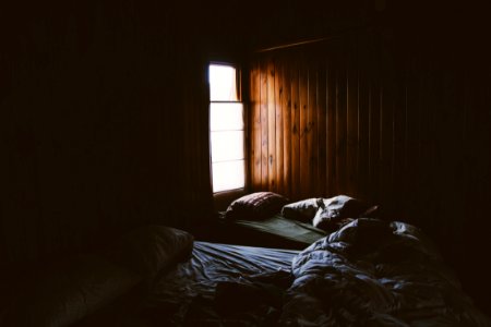 Pale light pouring into a cabin through a small window illuminates two unmade beds photo