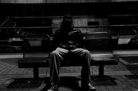 grayscale photography of man sitting down on metal bench