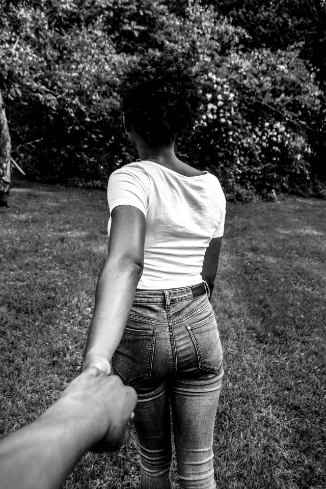 greyscale photography of woman walking with hand at the back holding other hand