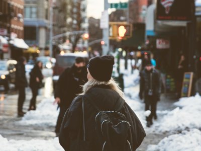 woman carrying backpack standing beside snow on street at daytime photo