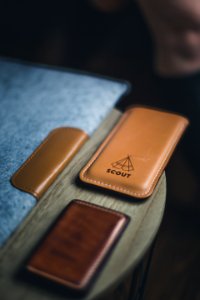 Leather laptop cover, wallet, and phone holder with a label that reads "SCOUT" on a wooden circular table photo