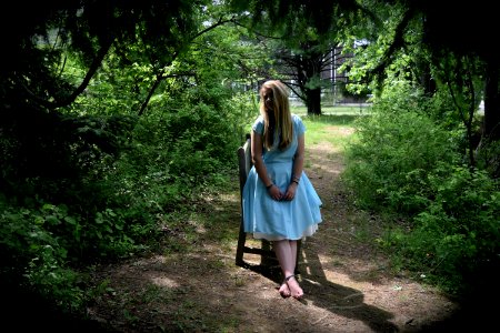 A young adult female in a white dress leaning on a chair in the middle of the woods. photo