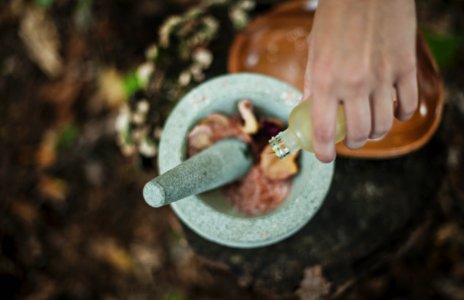 high angle photo of person pouring liquid from bottle inside mortar and pestle photo