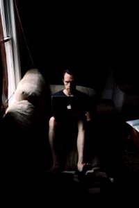 man seating on sofa using MacBook beside window photo