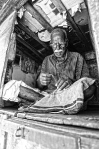 grayscale photo of man sewing textile while sitting on floor photo