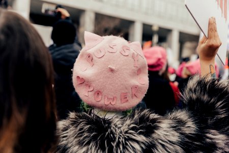 selective focus photography of person wearing pink fleece Pussy Power cap raising right hand photo