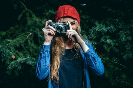 woman standing behind green leaf tree holding DSLR camera photo