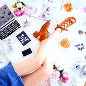 woman wearing brown open-toe chunky sandals sitting beside white smartphone, headphones and laptop