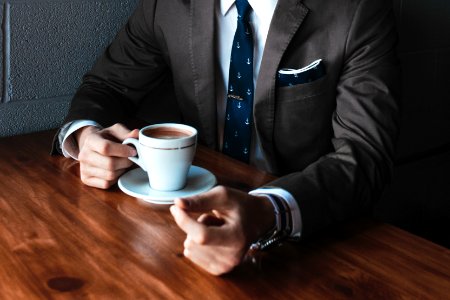 man holding cup filled with coffee on table photo