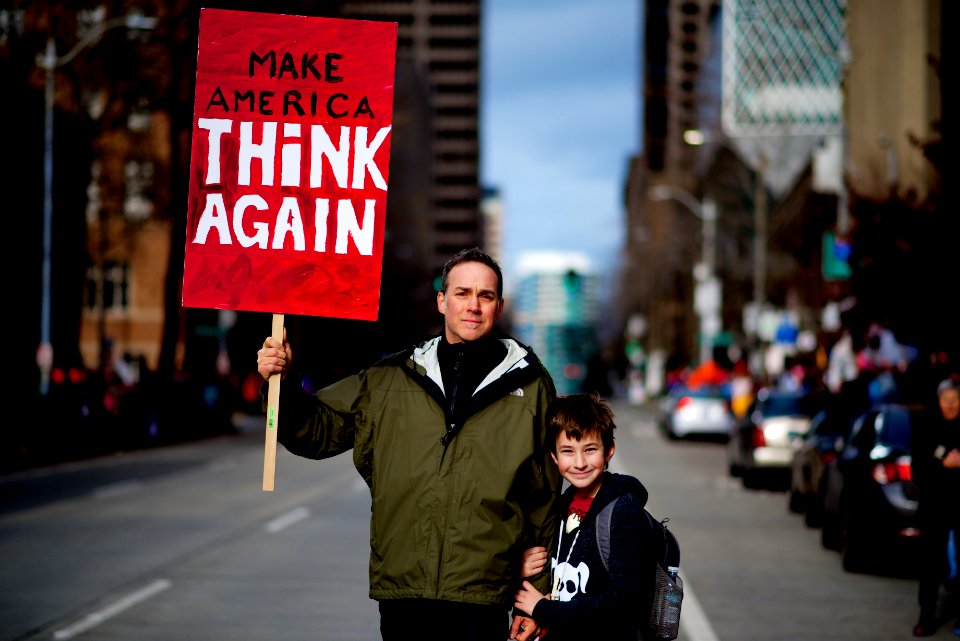 man beside boy holding red and white rally signage