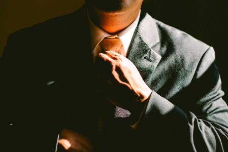 A man in a black suit loosening his tie photo