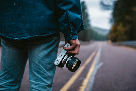 person holding gray and black camera while standing on road photo