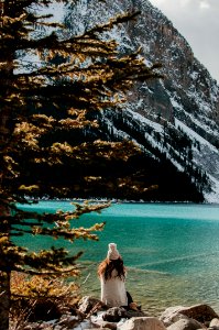 woman sitting on stone facing body of water and glacier mountain during day photo