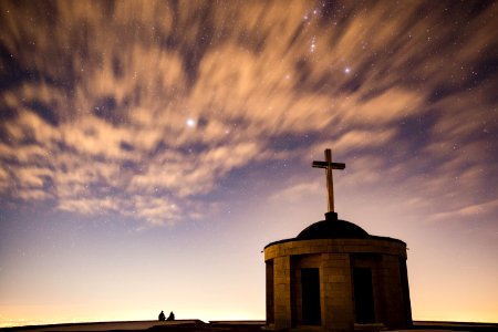 silhouette of brick cathedral with cross finial under blue sky photo