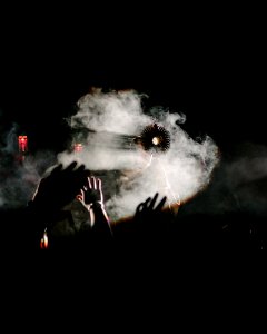 A religious object held up in front of a fog machine, with a crowd raising their hands.
