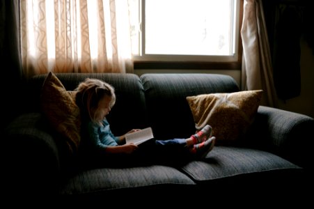 girl reading book sitting on sofa photo