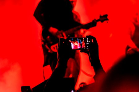 person holding smartphone in front of a person playing guitar on stage photo