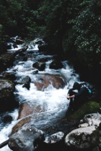 person wearing black hoodie sitting beside waterfalls photo