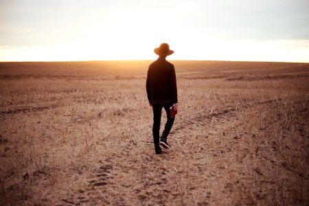 man walking on dried plain while looking towards the sun on horizon photo