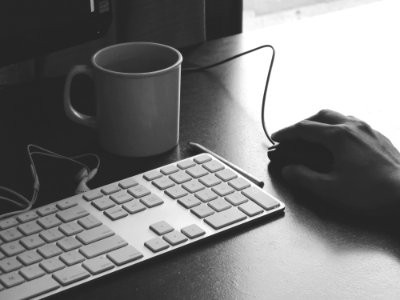 grayscale photography of person holding computer mouse near keyboard and mug photo