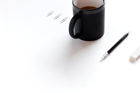 three white paper clips, black ceramic mug, black pencil, and white pencil eraser on white surface