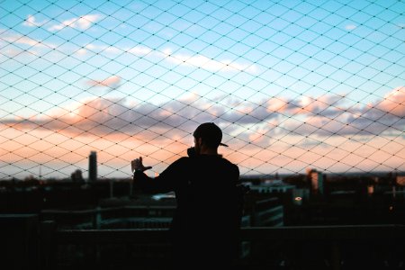 man standing behind chain link fence holding to fence during golden hour photo