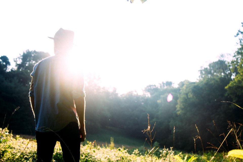 man standing on grass field with sun gazing