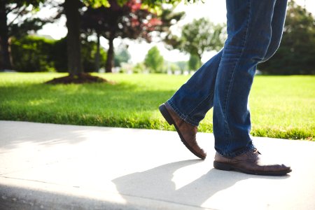 person wearing pair of brown shoes and blue denim jeans walking on concrete ground near green grass field during daytime photo