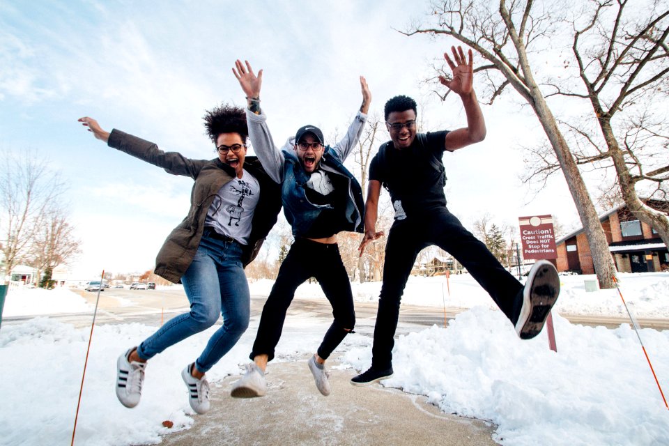 photo of three men jumping on ground near bare trees during daytime