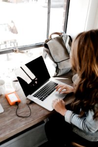 girl wearing grey long-sleeved shirt using MacBook Pro on brown wooden table