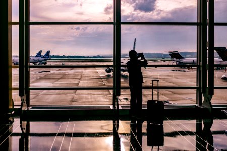 silhouette of person standing in front of glass while taking photo of plane photo