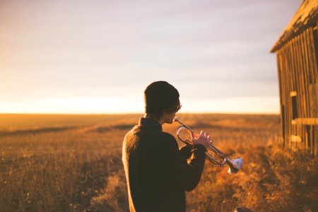 man playing trumpet outside house on field during daytime photo