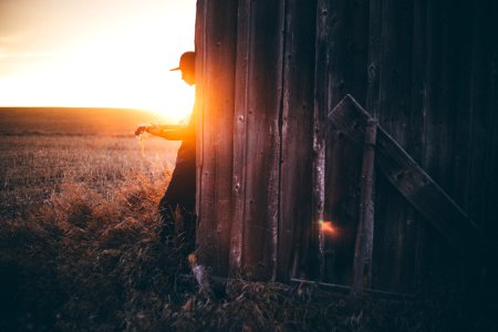 silhouette of man leaning on gray wooden house during sunset photo
