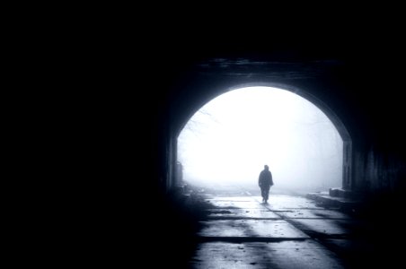 silhouette of person walking out from tunnel during daytime photo