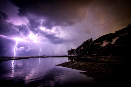 lightning near body of water and rock formation