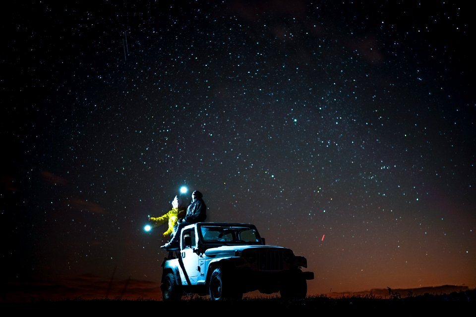 person sitting on top of wrangler under starry sky
