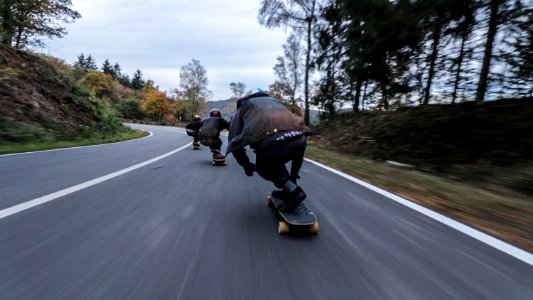 three person riding skateboards downhill during daytime photo