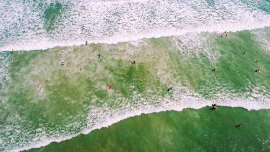 aerial photo of people on seashore with waves and bubbles at daytime photo