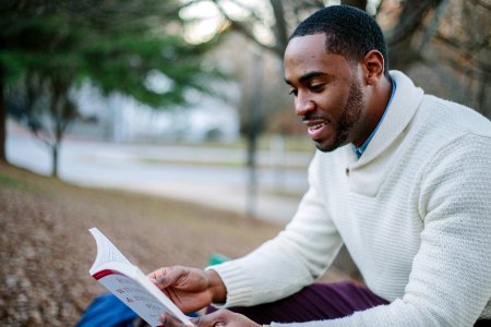 man wearing white sweater while reading book photo