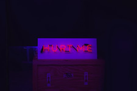 Red neon "Hurt Me" sign on top of a crate with arrow stickers photo