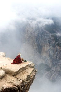 person sitting on cliff under cumulus cloud photo