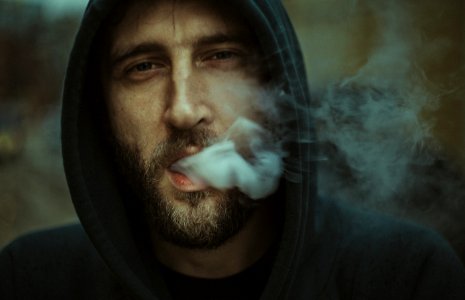 man wearing black pullover hoodie blowing white smoke